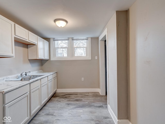 kitchen with a sink, baseboards, white cabinets, and light wood finished floors