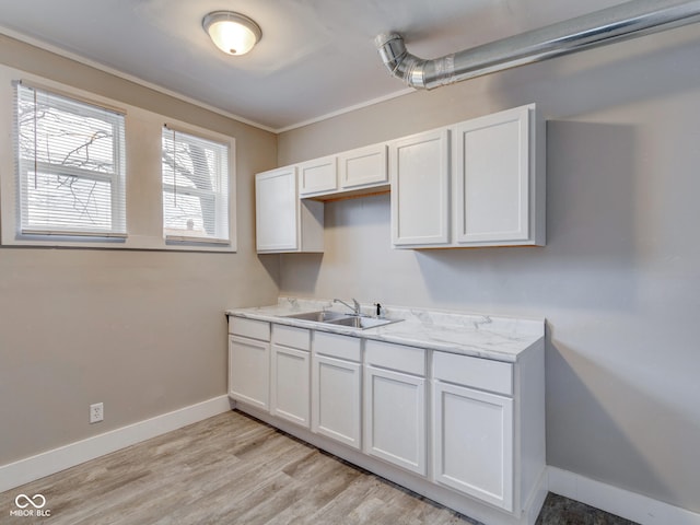 kitchen with white cabinets, baseboards, light wood-style floors, and a sink