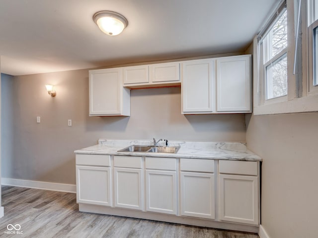 kitchen with white cabinetry, light wood-style floors, baseboards, and a sink