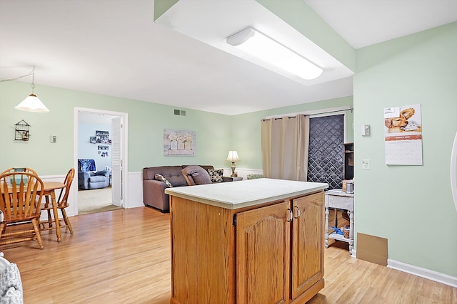 kitchen with light wood-style flooring, a kitchen island, open floor plan, light countertops, and decorative light fixtures