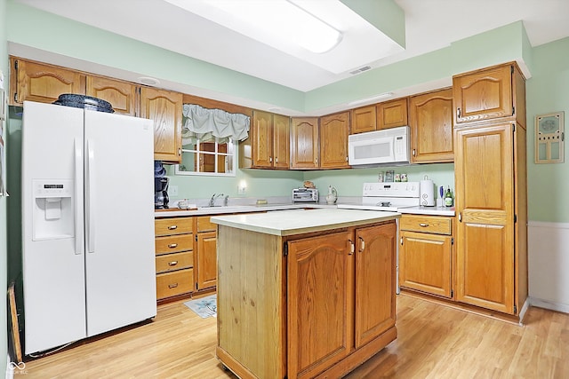 kitchen with a center island, brown cabinets, light countertops, light wood-style floors, and white appliances