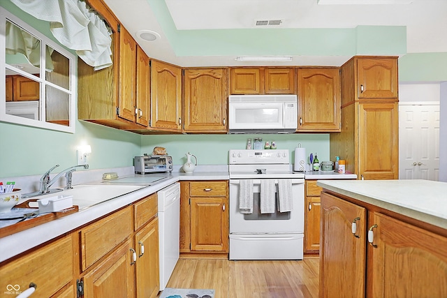 kitchen with white appliances, a sink, visible vents, light countertops, and brown cabinetry