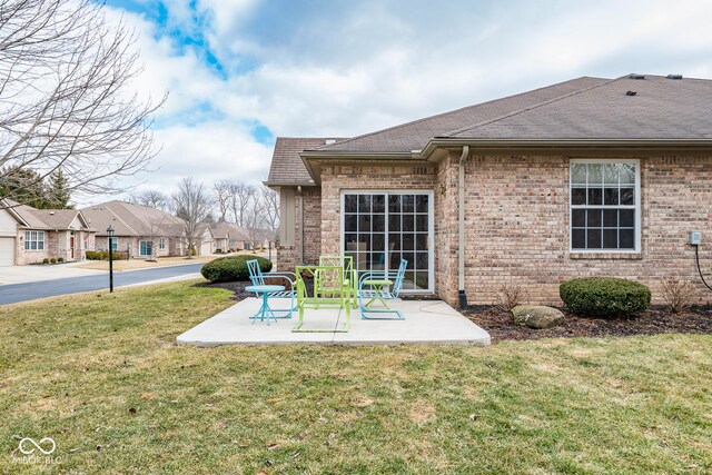 back of property with a yard, roof with shingles, a patio, and brick siding