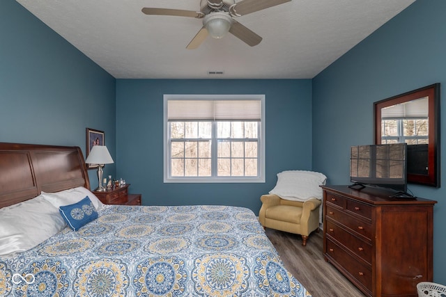 bedroom featuring a ceiling fan, visible vents, and wood finished floors