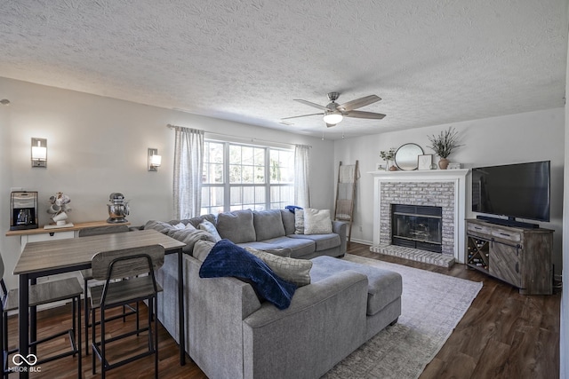 living area featuring dark wood finished floors, a brick fireplace, a textured ceiling, and ceiling fan