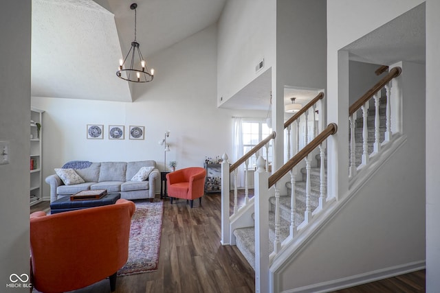 living room featuring wood finished floors, visible vents, high vaulted ceiling, an inviting chandelier, and stairs