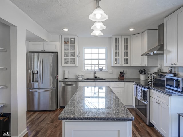 kitchen with a kitchen island, a sink, appliances with stainless steel finishes, white cabinetry, and wall chimney exhaust hood