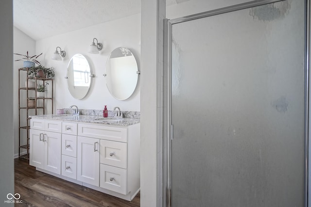 full bath featuring a textured ceiling, wood finished floors, a stall shower, and a sink