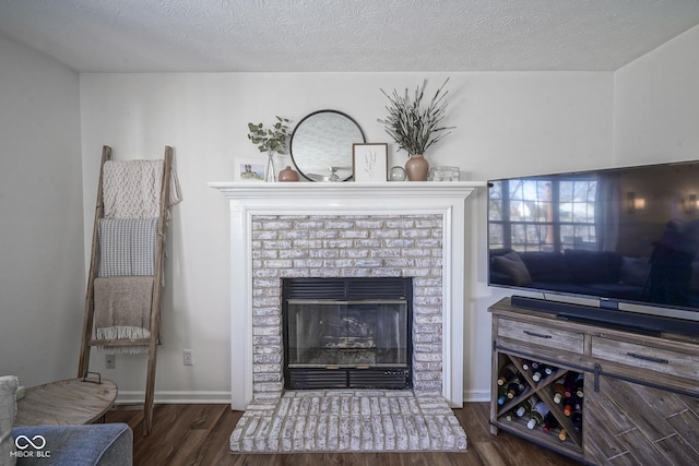 living area with a brick fireplace, a textured ceiling, baseboards, and wood finished floors