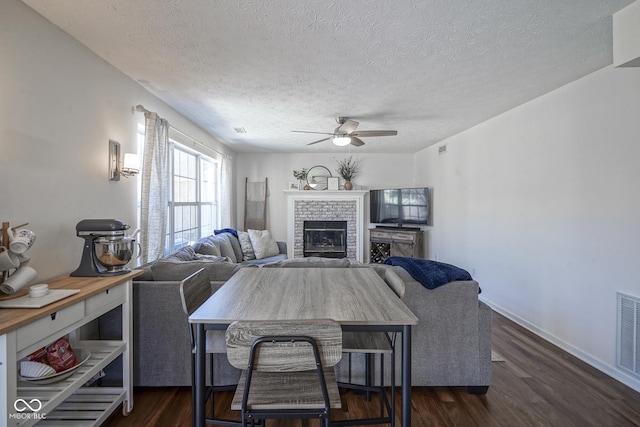 living area with dark wood-type flooring, a brick fireplace, a ceiling fan, and a textured ceiling