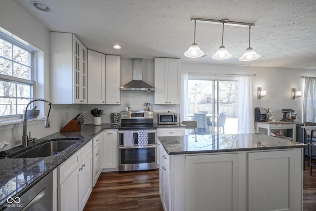 kitchen with a sink, dark wood-style floors, stainless steel appliances, dark stone counters, and wall chimney range hood