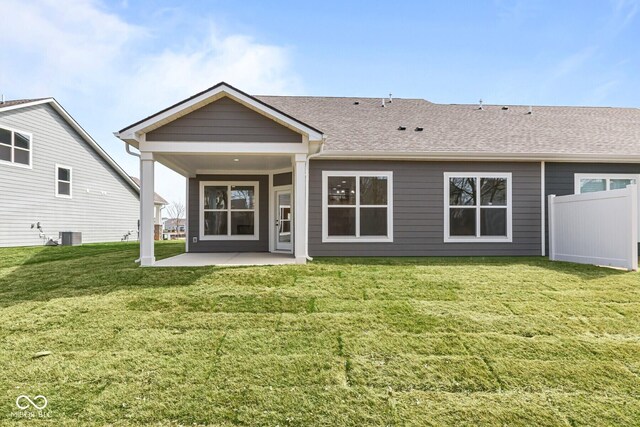 rear view of property featuring roof with shingles, a lawn, fence, and a patio