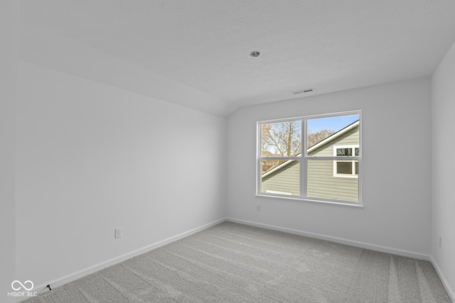carpeted empty room with a textured ceiling, baseboards, lofted ceiling, and visible vents