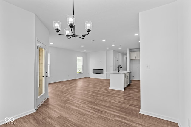 unfurnished living room featuring an inviting chandelier, a sink, light wood-style floors, and recessed lighting
