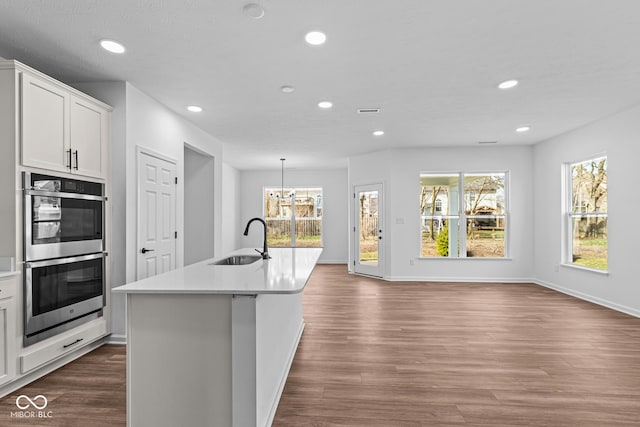 kitchen featuring light countertops, stainless steel double oven, recessed lighting, dark wood-type flooring, and a sink