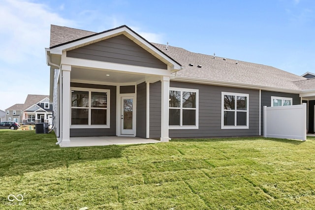 rear view of house featuring cooling unit, a shingled roof, a patio area, and a yard