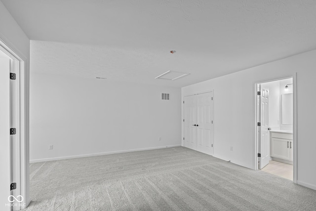 unfurnished room featuring a textured ceiling, visible vents, baseboards, attic access, and light carpet
