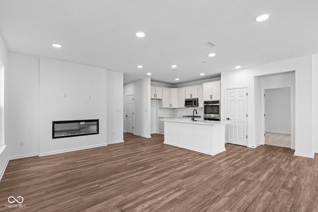 kitchen with a sink, stainless steel microwave, recessed lighting, and dark wood finished floors