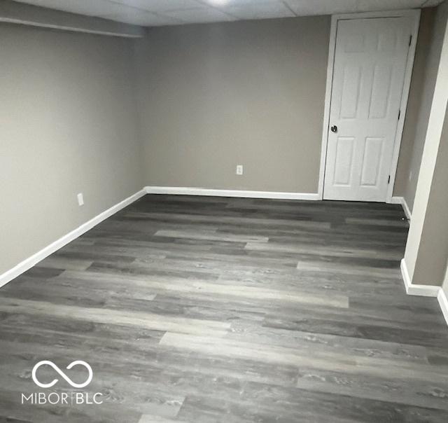 finished below grade area featuring wood finished floors, a paneled ceiling, and baseboards