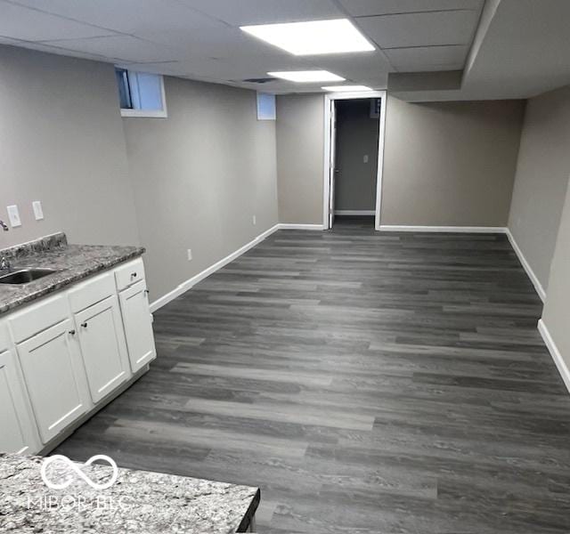 finished basement featuring a sink, a drop ceiling, dark wood finished floors, and baseboards