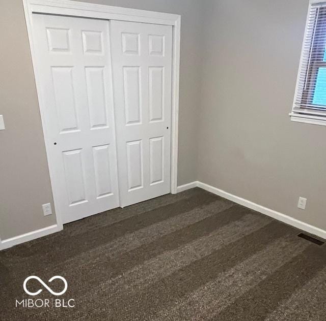 unfurnished bedroom featuring a closet, dark wood finished floors, and baseboards