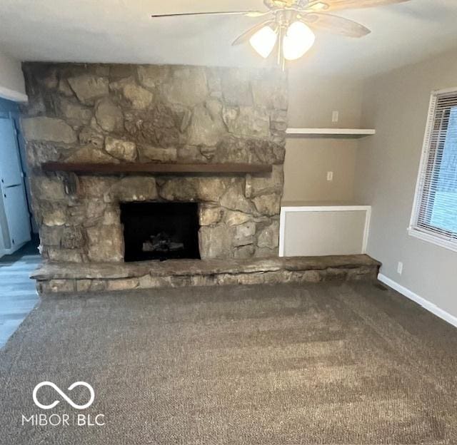 unfurnished living room featuring ceiling fan, a stone fireplace, and baseboards