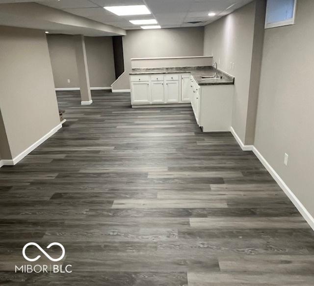 finished below grade area with dark wood-type flooring, baseboards, a drop ceiling, and a sink