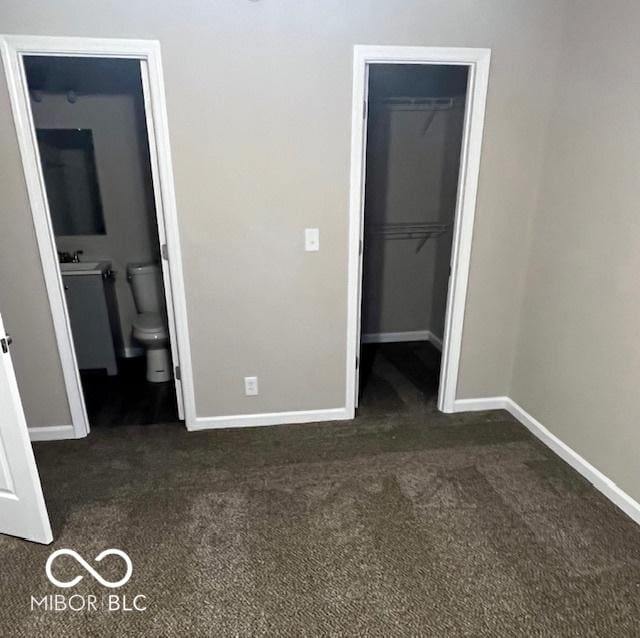 unfurnished bedroom with dark colored carpet, a closet, a spacious closet, a sink, and baseboards