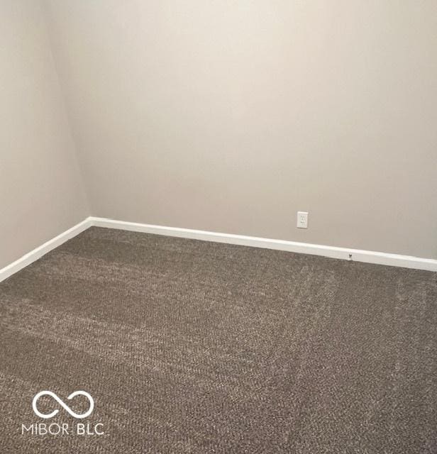 unfurnished room featuring dark carpet and baseboards