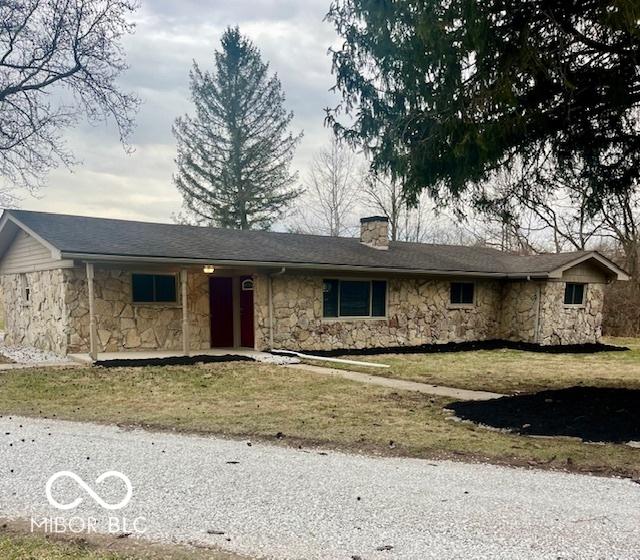 single story home featuring stone siding, a chimney, and a front yard