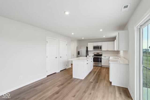 kitchen with a kitchen island, stainless steel appliances, light countertops, light wood-style floors, and a sink