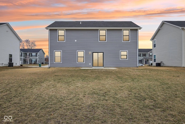 back of house at dusk with central air condition unit and a lawn