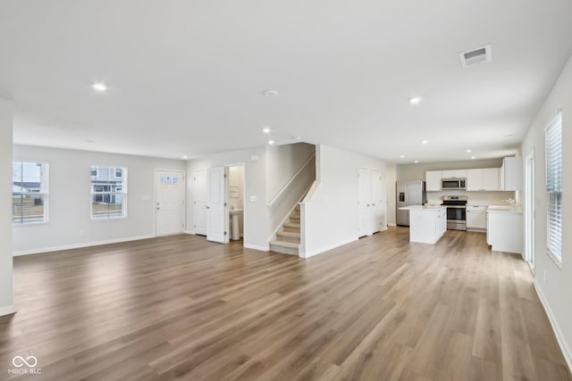 unfurnished living room featuring recessed lighting, visible vents, light wood-style floors, baseboards, and stairs