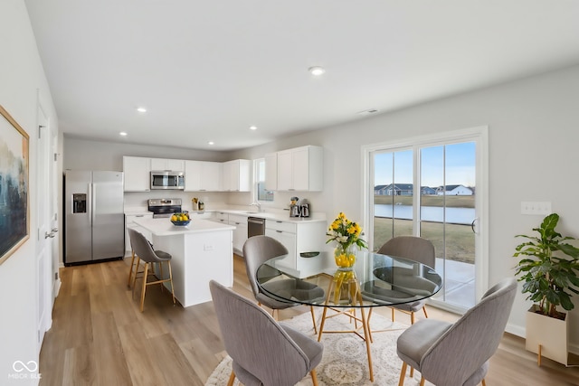 dining room with a water view, light wood-style floors, and recessed lighting