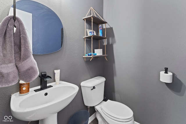 half bath featuring a textured wall, baseboards, a sink, and toilet