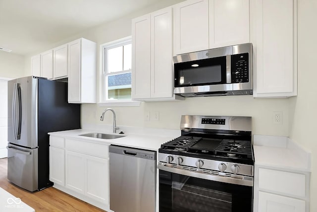 kitchen featuring light wood finished floors, white cabinets, appliances with stainless steel finishes, light countertops, and a sink