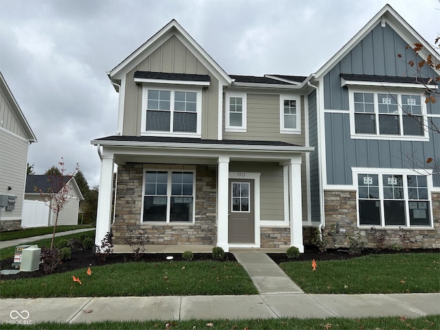 view of front of house featuring board and batten siding, a front yard, stone siding, and a porch