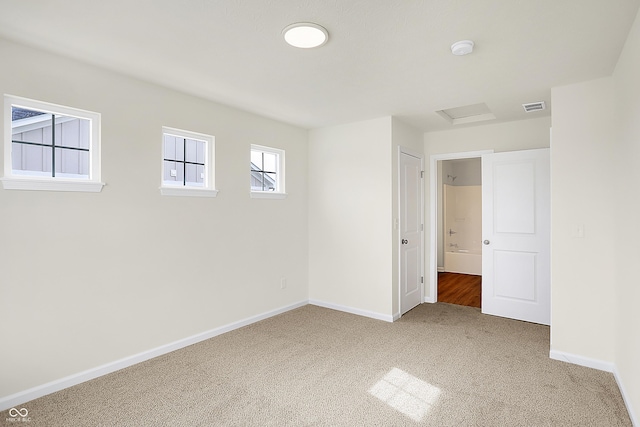 carpeted spare room with baseboards, visible vents, and attic access