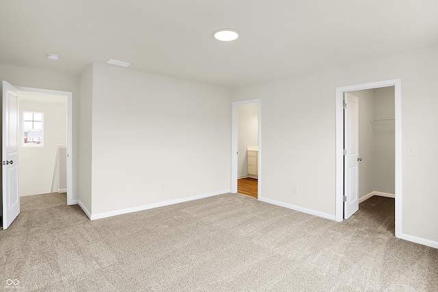 unfurnished bedroom featuring a closet, a spacious closet, baseboards, and carpet flooring