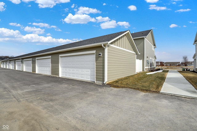 view of side of home featuring a shingled roof, board and batten siding, and community garages