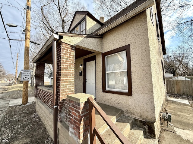 view of exterior entry with brick siding, fence, and stucco siding