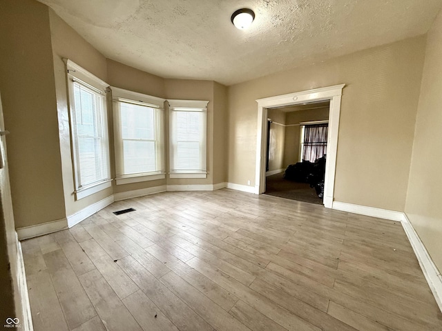 unfurnished room with a textured ceiling, wood finished floors, visible vents, and baseboards