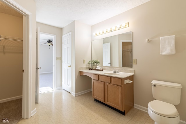 bathroom featuring a spacious closet, toilet, vanity, a textured ceiling, and baseboards