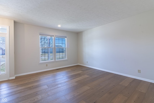 empty room with dark wood-style floors, a textured ceiling, visible vents, and baseboards