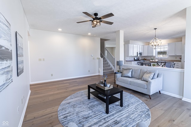 living room featuring light wood-style floors, stairway, baseboards, and ceiling fan with notable chandelier