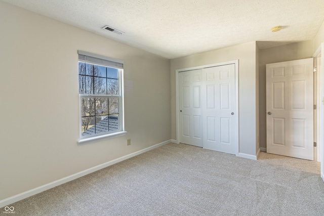 unfurnished bedroom featuring a textured ceiling, light colored carpet, visible vents, baseboards, and a closet