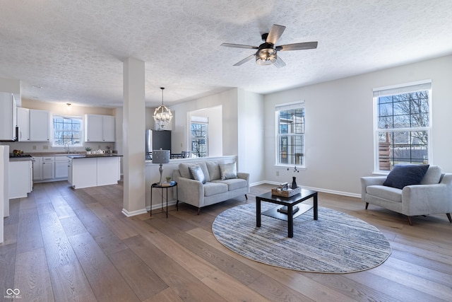 living room with a textured ceiling, baseboards, wood finished floors, and ceiling fan with notable chandelier