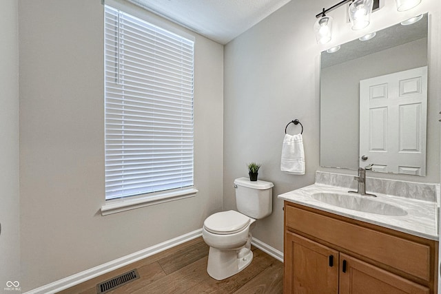 bathroom featuring baseboards, visible vents, toilet, wood finished floors, and vanity