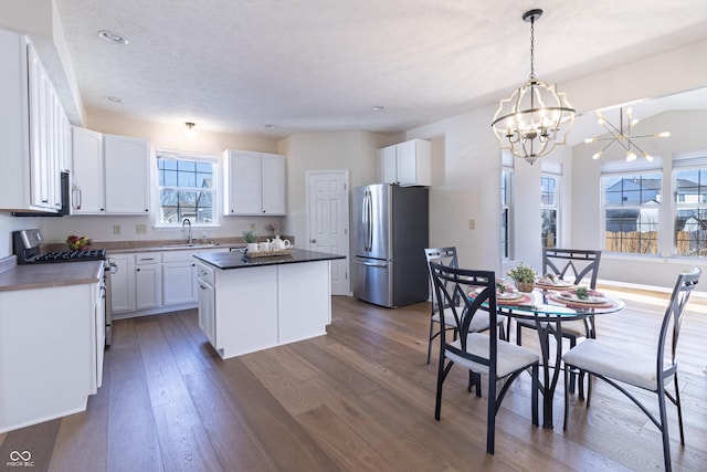 kitchen with stainless steel appliances, wood finished floors, a sink, a center island, and dark countertops