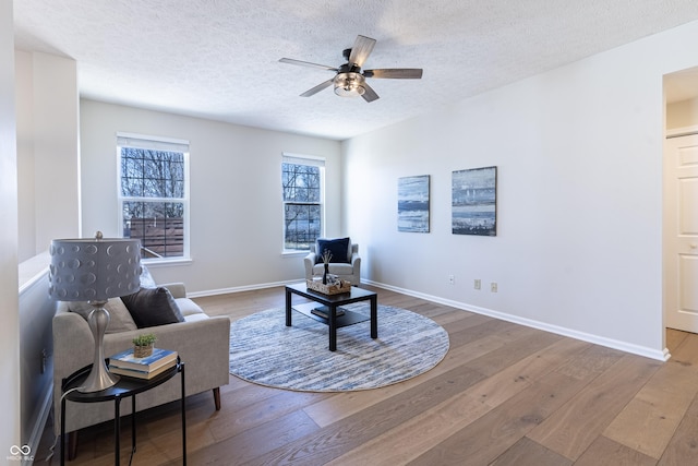 living area featuring ceiling fan, a textured ceiling, baseboards, and wood finished floors